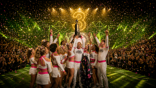 Black Diamonds cheer team celebrating a third consecutive championship win on a competition stage with trophy, confetti, neon green lights, and gold championship lighting.